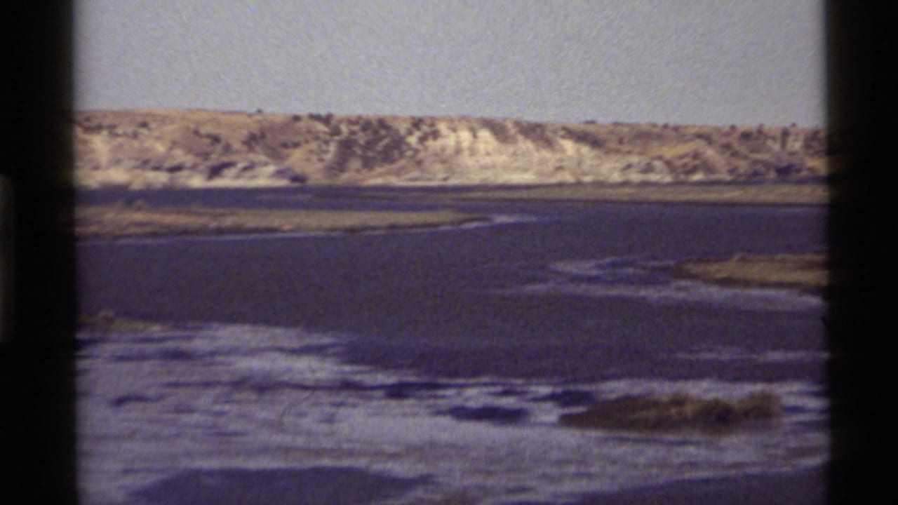 Calm lake water with rippled shallows and a sunlit hillside beyond.