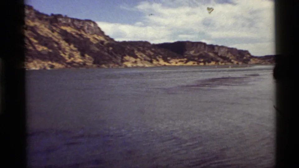 Holland Lake in Montana appears across a wide 8mm frame, with rippled water, layered rock slopes, and a pale clouded sky.