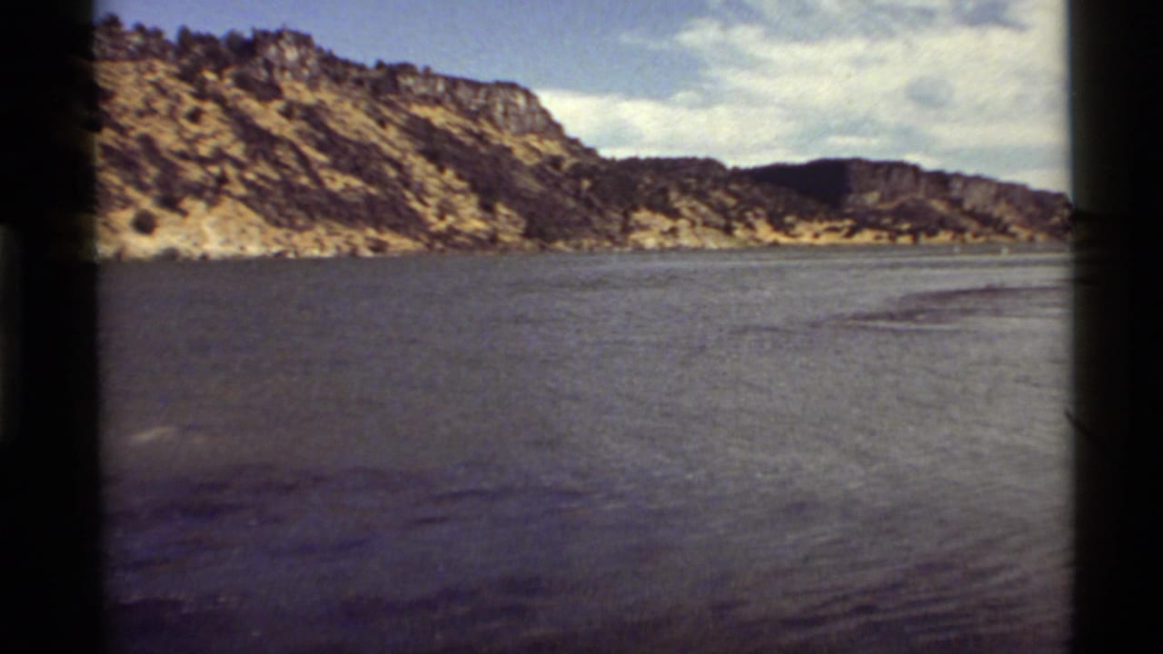 1972 8mm view at Holland Lake, Montana, showing calm water with rocky cliffs and daylight sky.
