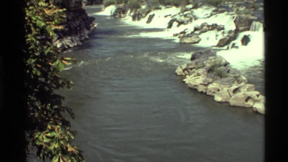 Home-movie frame from Holland Lake, Montana in 1972, with white rapids, rippled water, rocks, and foliage along the bank.