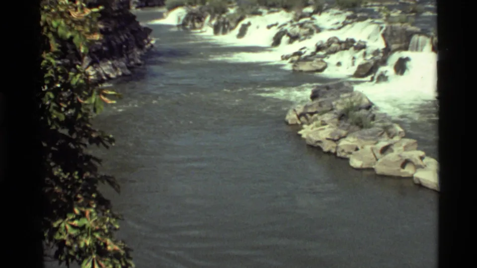 1972 8mm frame at Holland Lake, Montana, showing white water over rocks with foliage along the edge and calmer water below.