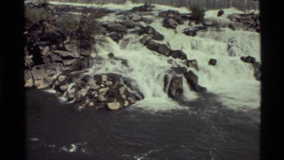 Broad white-water cascade at Holland Lake, Montana, flowing over layered rocks into a darker stream channel.