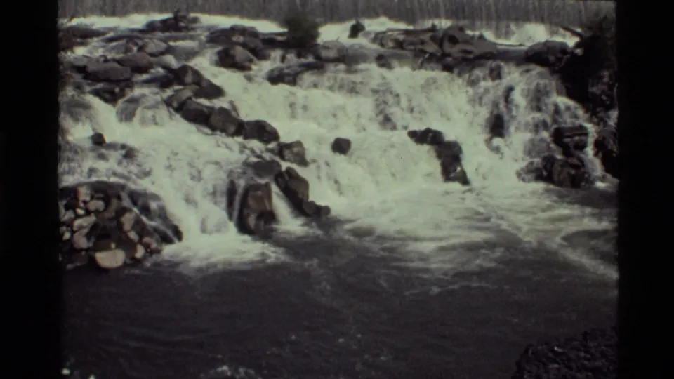 8mm home-movie frame from Holland Lake, Montana, with foaming water pouring across uneven rocks.