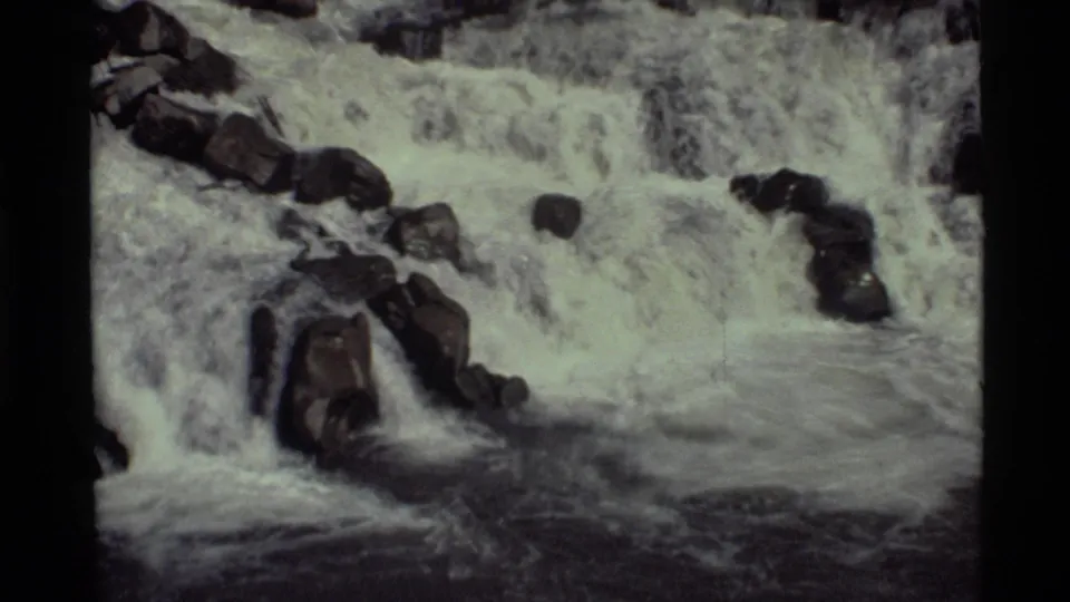 Closer 1972 Holland Lake frame with frothy waterfall flow surrounding large dark rocks in the channel.
