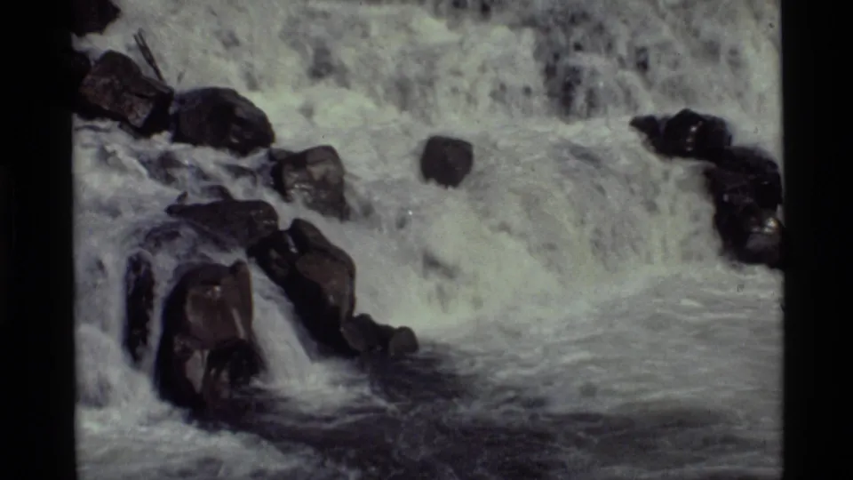Tight 8mm view of the Holland Lake waterfall, showing foaming water and dark rocks near the lower pool.