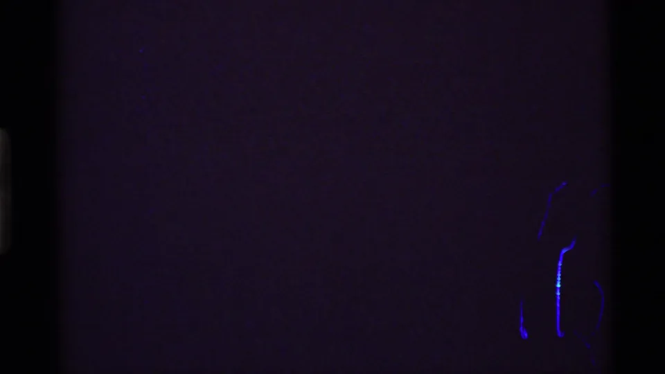 A mostly dark 8mm frame with faint purple tone and small blue marks near the lower right, likely near the reel end.