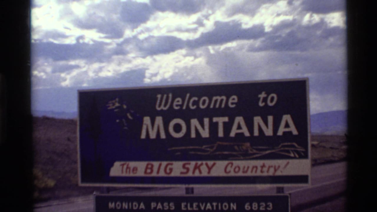 1972 8mm frame of a Montana welcome sign reading Big Sky Country with Monida Pass elevation panel below.