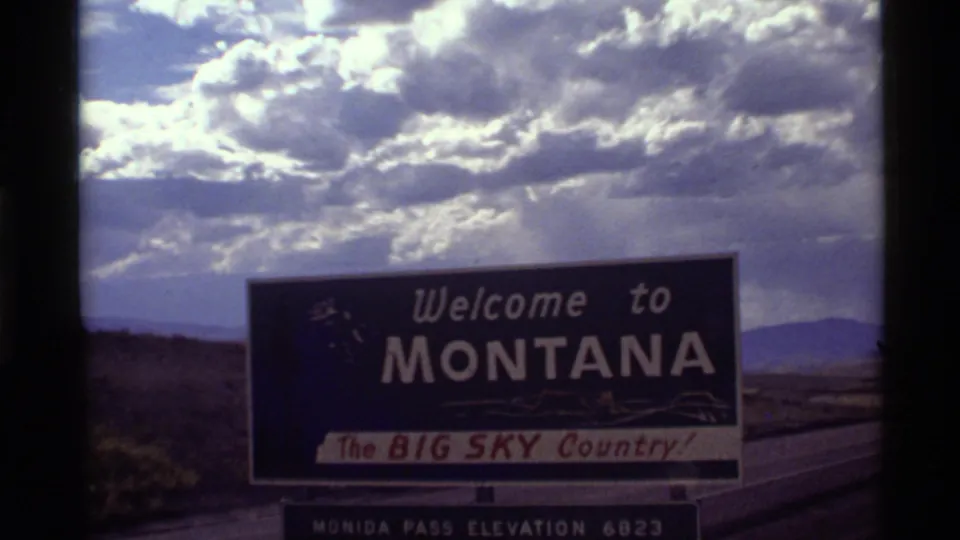 1972 Montana roadside welcome sign with Big Sky Country slogan, seen from a home-movie road-trip viewpoint.