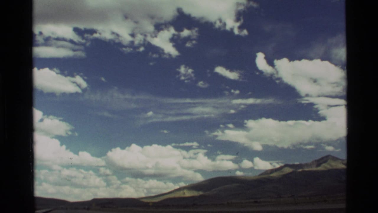 Wide blue sky with scattered white clouds above a dark mountain horizon.