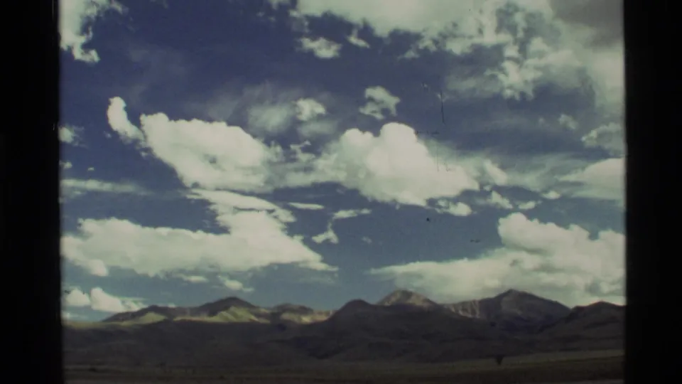 1972 home-movie landscape frame with dark low terrain, mountain ridges, and large cloud forms over rural Montana.