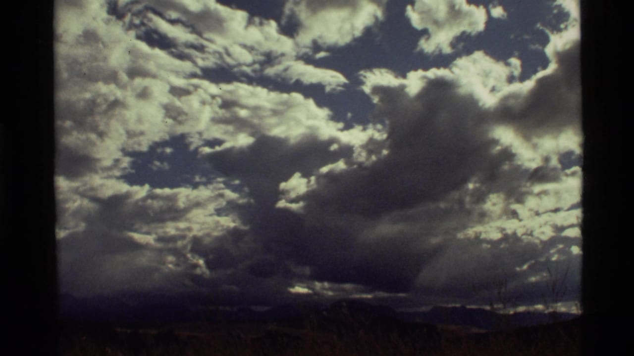 1972 8mm view near Holland Lake, Montana, with heavy clouds, blue sky gaps, and a dark distant horizon.