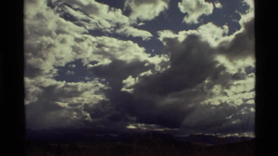 1972 8mm view near Holland Lake, Montana, with heavy clouds, blue sky gaps, and a dark distant horizon.