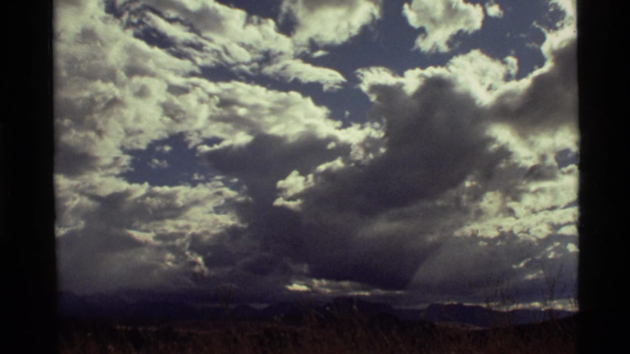 Home-movie frame from Holland Lake, Montana, showing a large gray cloud bank under bright white clouds in a blue sky.