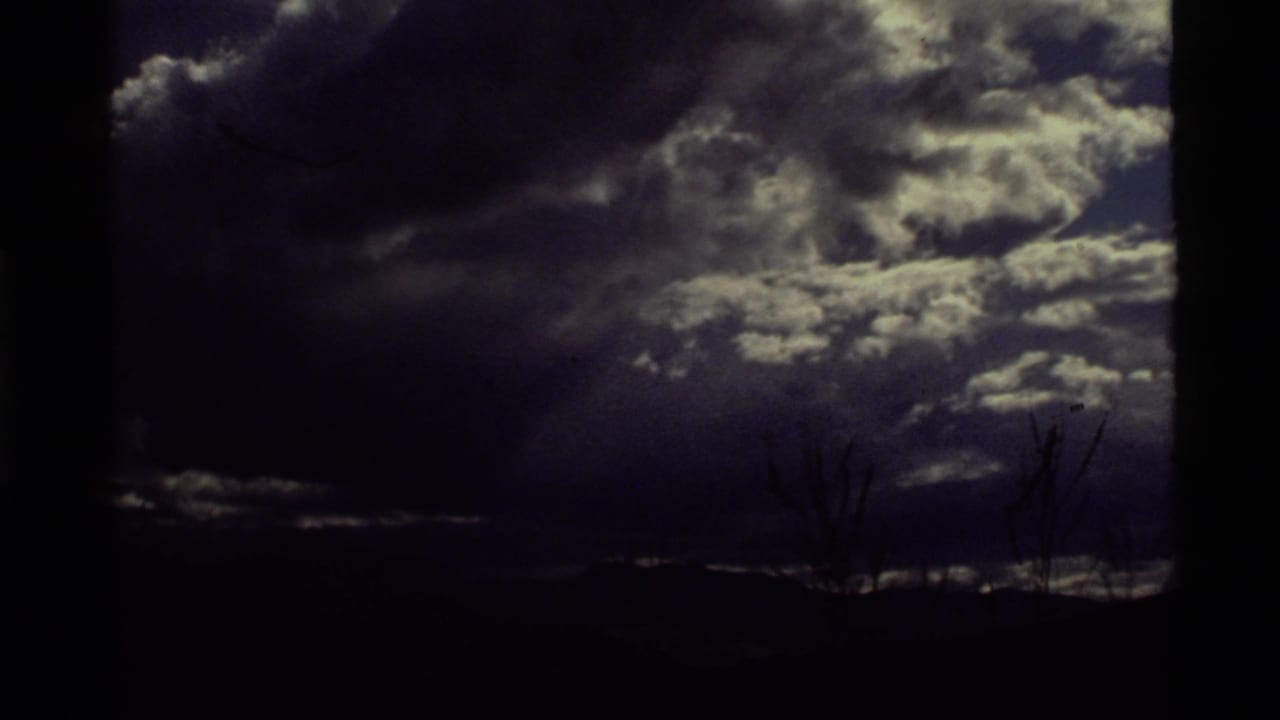 Dark storm clouds over a low mountain horizon with silhouetted bare branches.