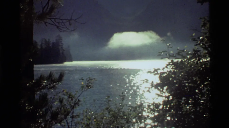 1972 8mm view of Holland Lake with a luminous cloud over the water, strong reflection, and shaded trees framing the scene.