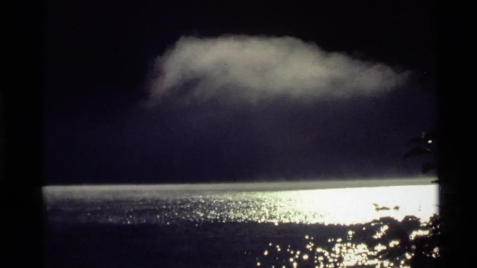 1972 Holland Lake, Montana 8mm frame showing dark water, bright reflected light, a low cloud or mist bank, and shadowed shoreline foliage.