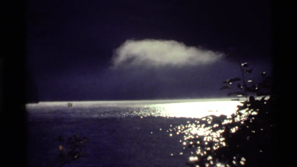 1972 Holland Lake, Montana frame with a luminous band on the lake, a pale low cloud, dark sky, and tree silhouettes along the right edge.