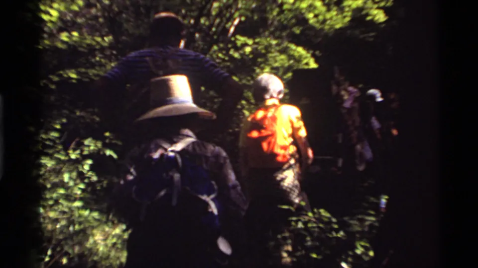 Backpackers on a wooded trail near Holland Lake, Montana, filmed from behind in 1972 8mm footage.