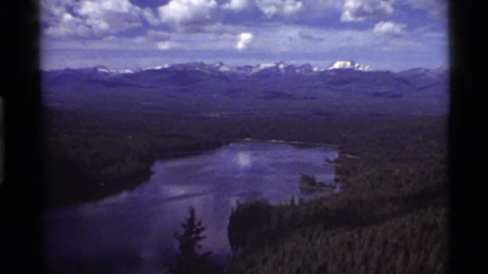 The final frame of the Holland Lake view holds a distant mountain skyline, reflective lake water, conifer forest, and visible 8mm edge darkening.