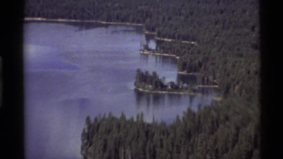 1972 Holland Lake aerial showing small tree-covered islands, calm water, and dense evergreen forest around the shore.
