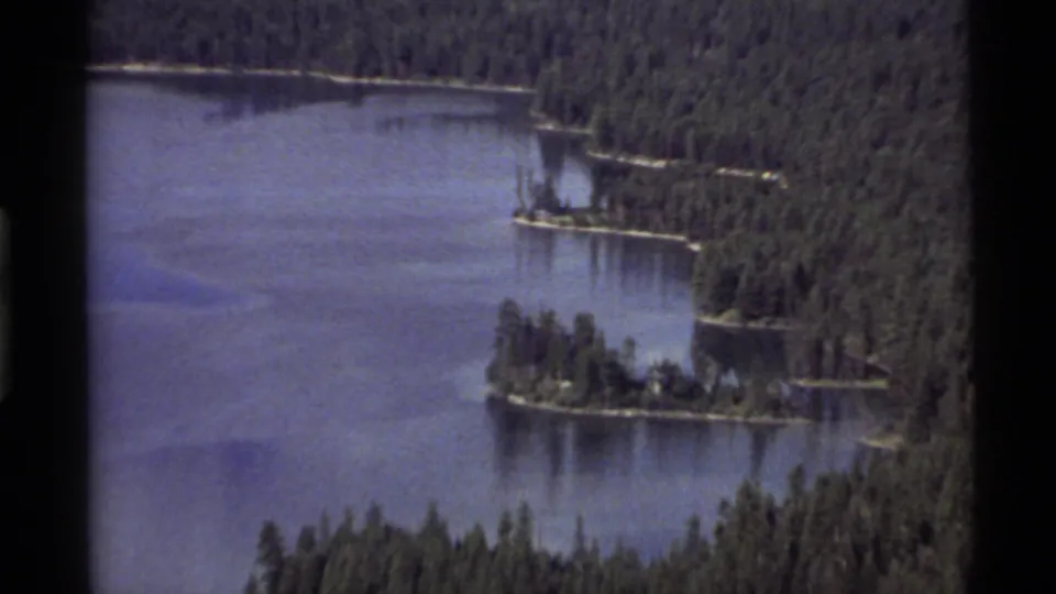 1972 8mm view of Holland Lake, Montana, showing blue water, evergreen shoreline, and small wooded islands.