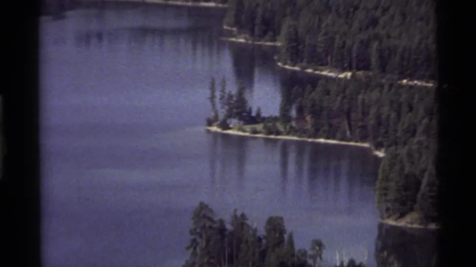 Aerial-style 8mm view of Holland Lake with evergreen shoreline, small island points, and calm blue water.