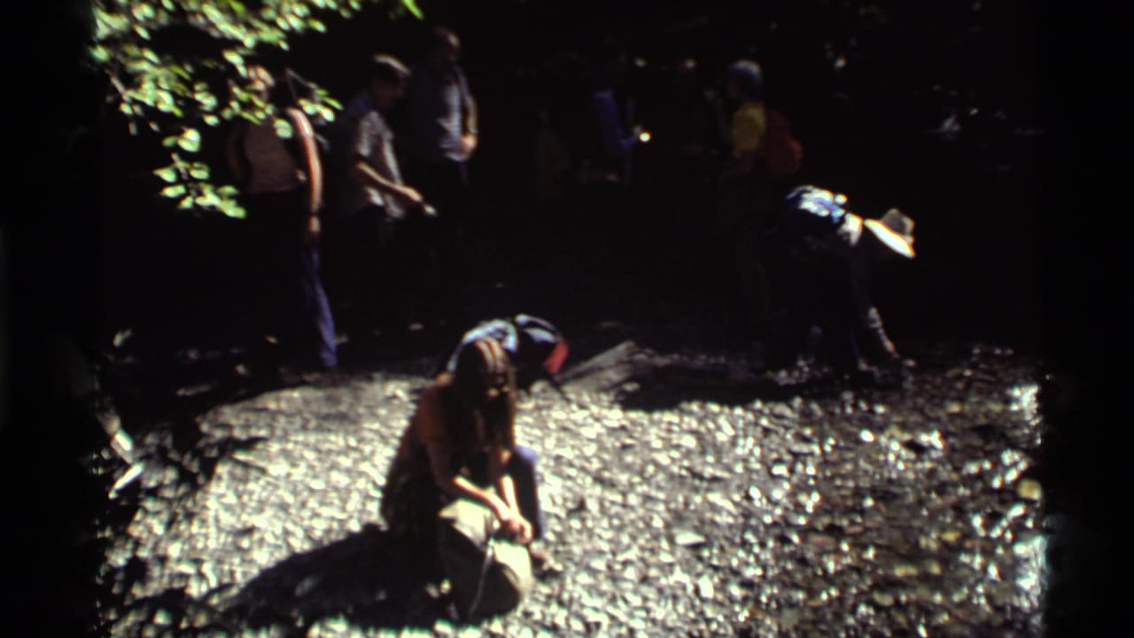 1972 8mm Holland Lake footage shows hikers in shade beside a rocky spring area as a woman kneels to drink.