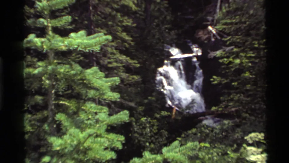 A wider handheld 8mm view shows the Holland Lake area waterfall surrounded by dense evergreen growth.