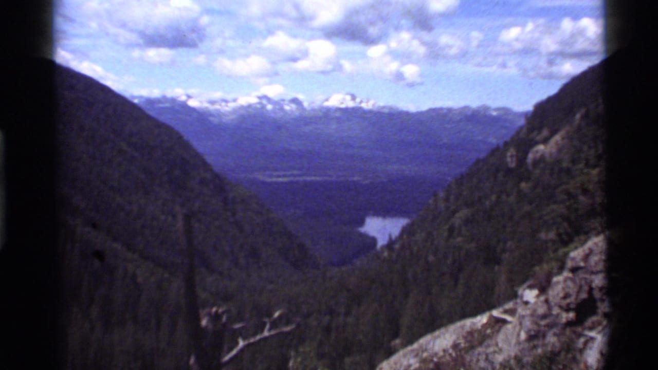Mountain valley panorama with lake water visible between forested slopes.