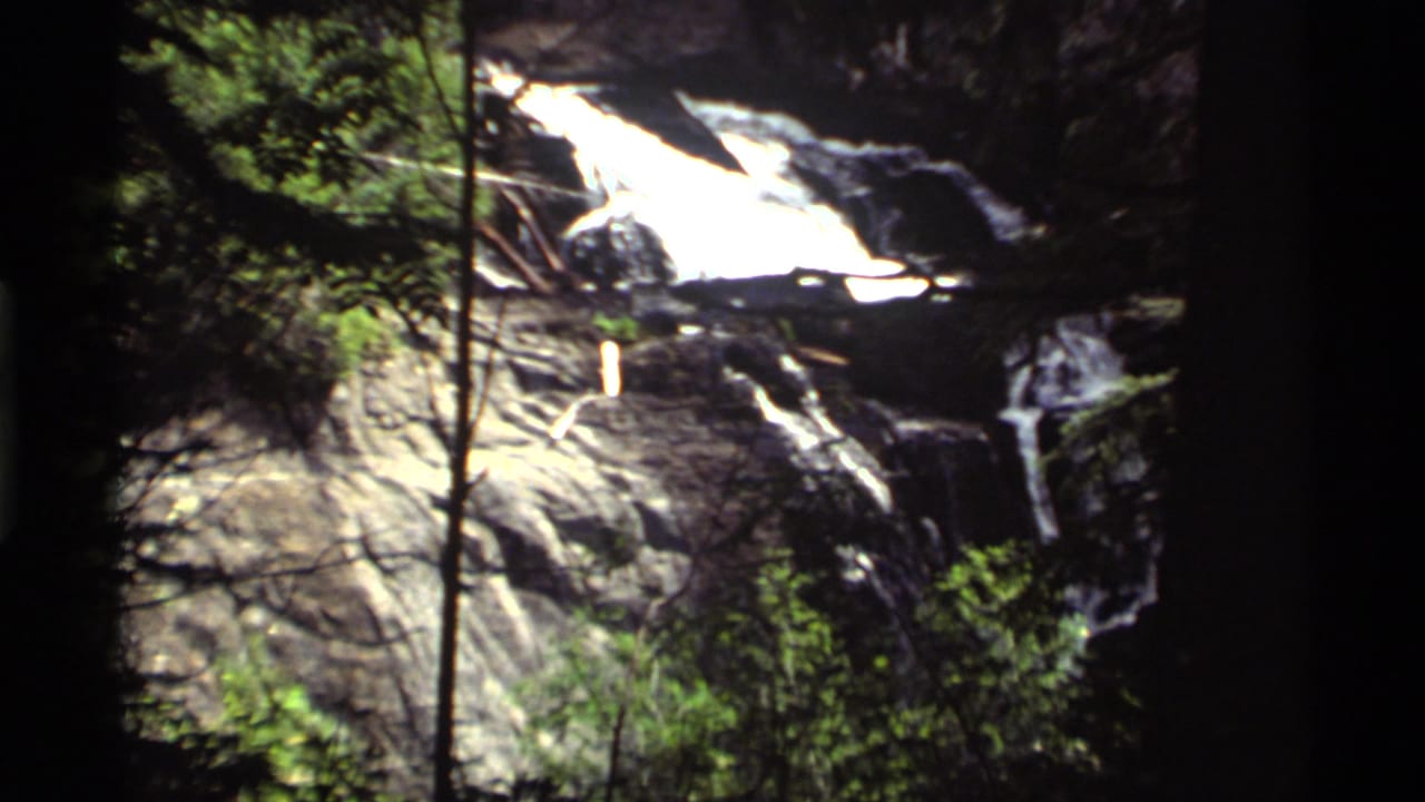 Bright waterfall flowing over dark rocks with trees at the edge of the frame.