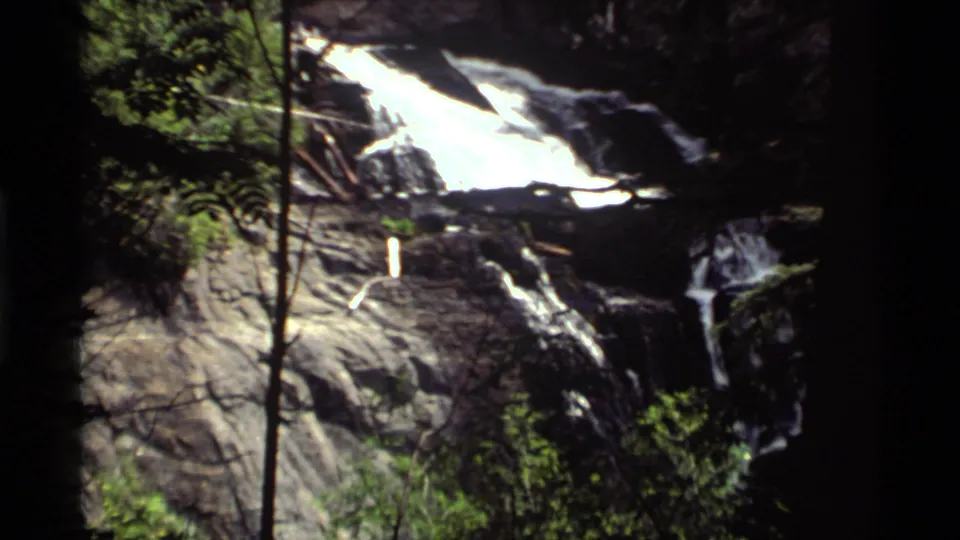 Close 1972 Holland Lake, Montana home-movie view of white waterfall water moving across dark rocks and trees.