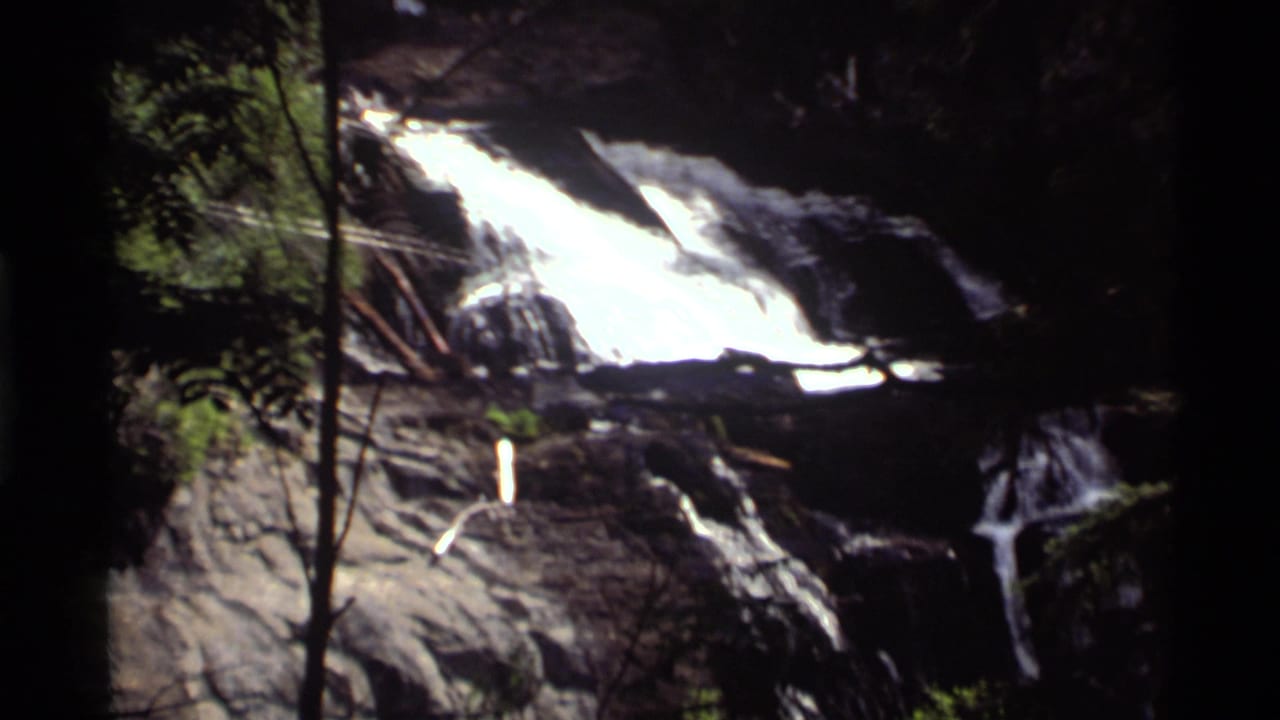 1972 Holland Lake, Montana 8mm frame showing a bright waterfall spilling over rocky ledges in dense forest shade.