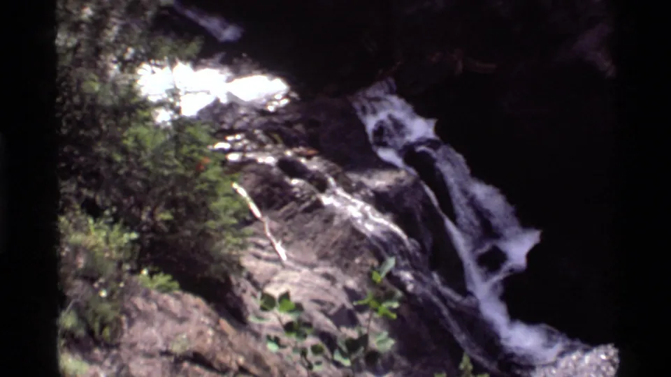 1972 Holland Lake, Montana 8mm frame showing a narrower waterfall chute running down dark rocks through forest shade.
