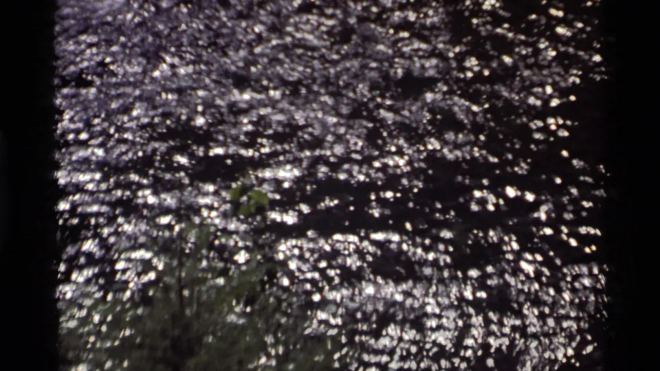 1972 8mm view at Holland Lake focused on bright, wind-rippled water and nearby shoreline vegetation.