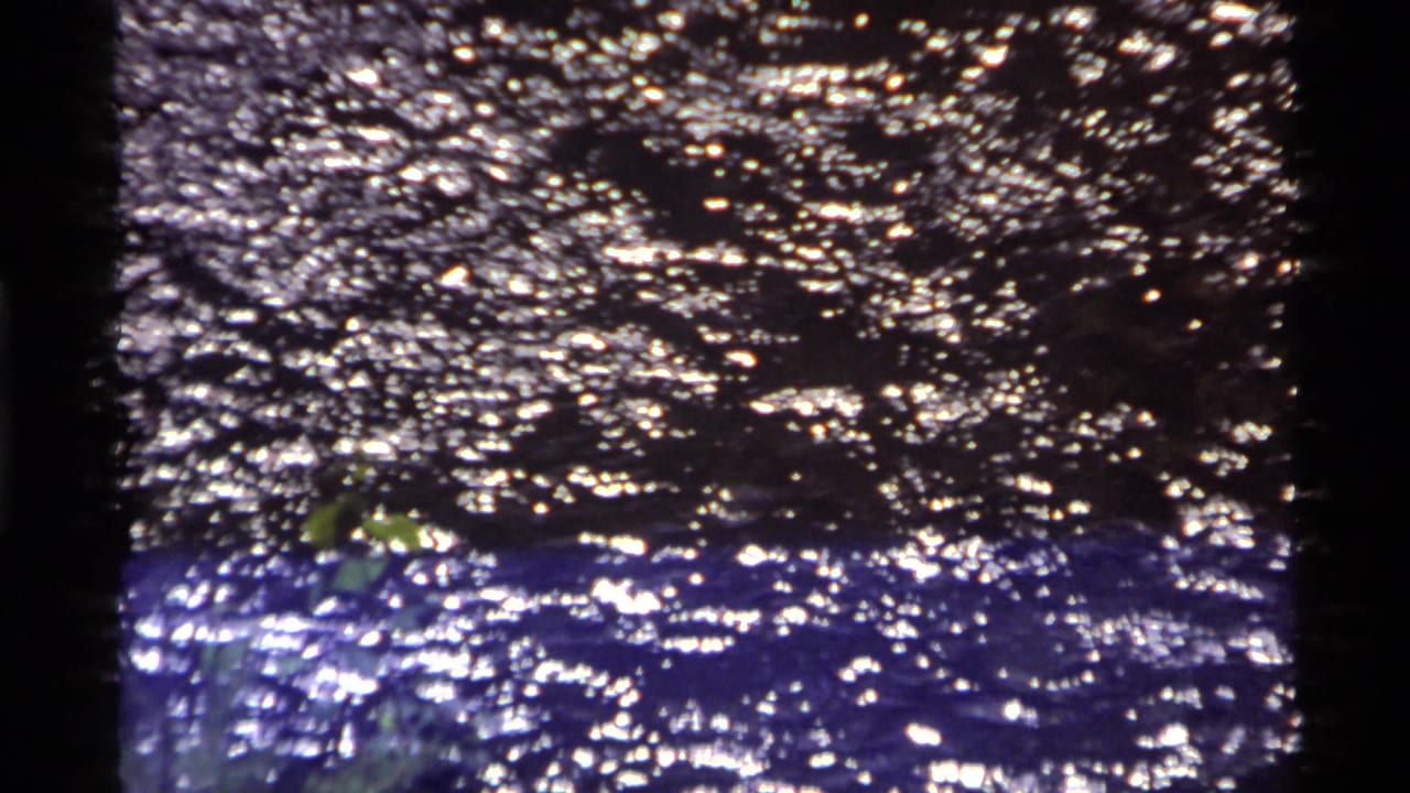 Rippling water catches bright reflections in 1972 Holland Lake home-movie footage, framed tightly with a dark film edge.