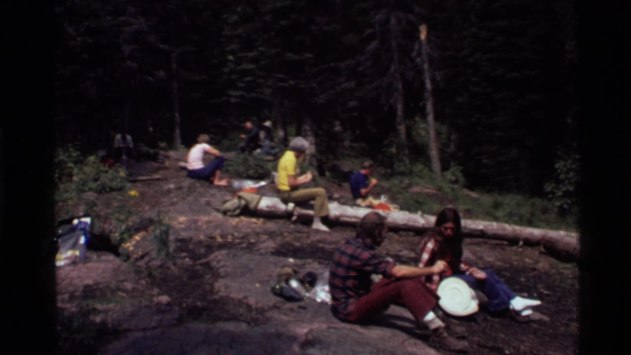 People seated in a forest clearing near a fallen log during a camping stop.