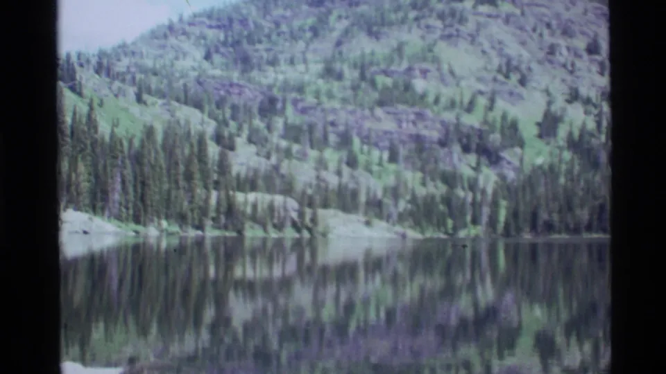 A wooded slope above Holland Lake is mirrored in still water, with soft 8mm exposure and muted green tones.