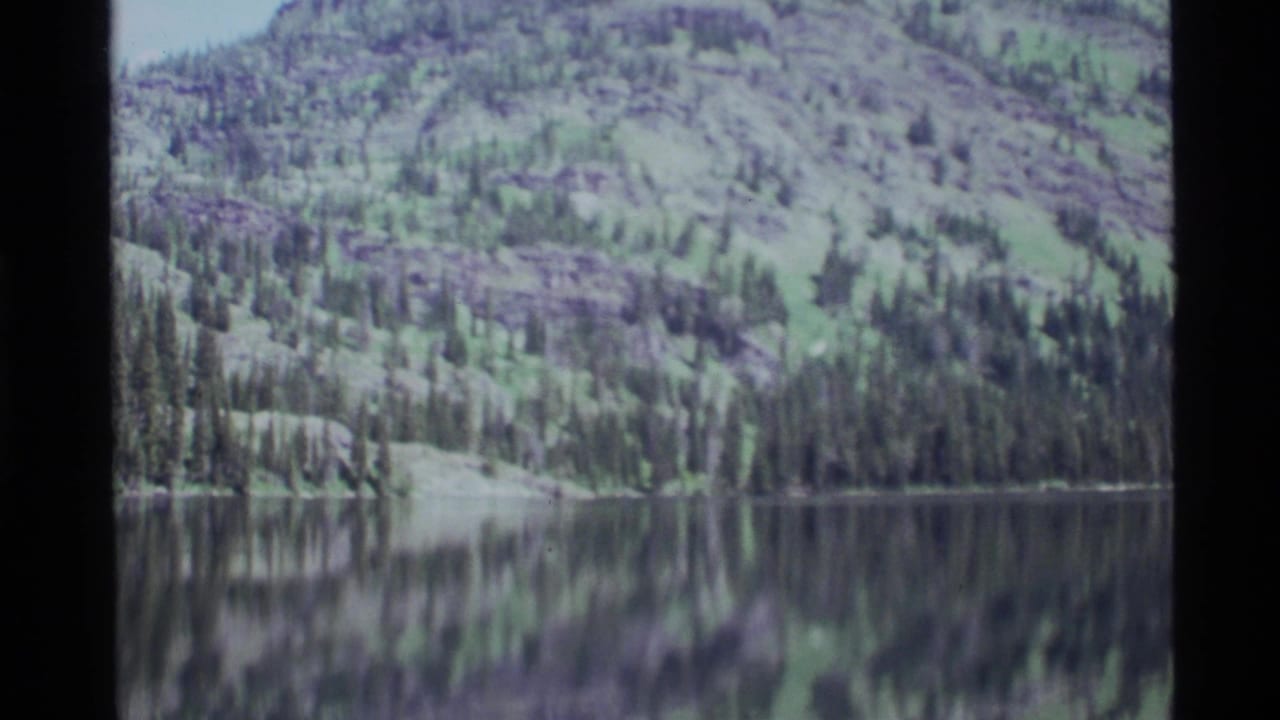 1972 8mm view at Holland Lake, Montana, with forested mountain slopes reflected in still water.