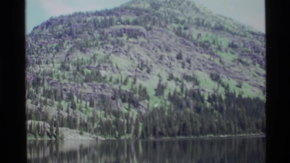 Wide 8mm landscape frame of Holland Lake, Montana, showing green mountain terrain and dark lake reflections.