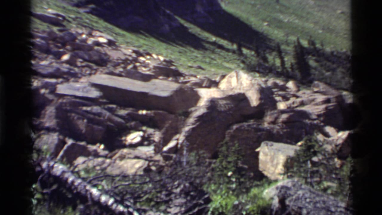 1972 8mm frame at Holland Lake, Montana showing boulders, grass, debris, and a dark foreground edge during a landscape pan.