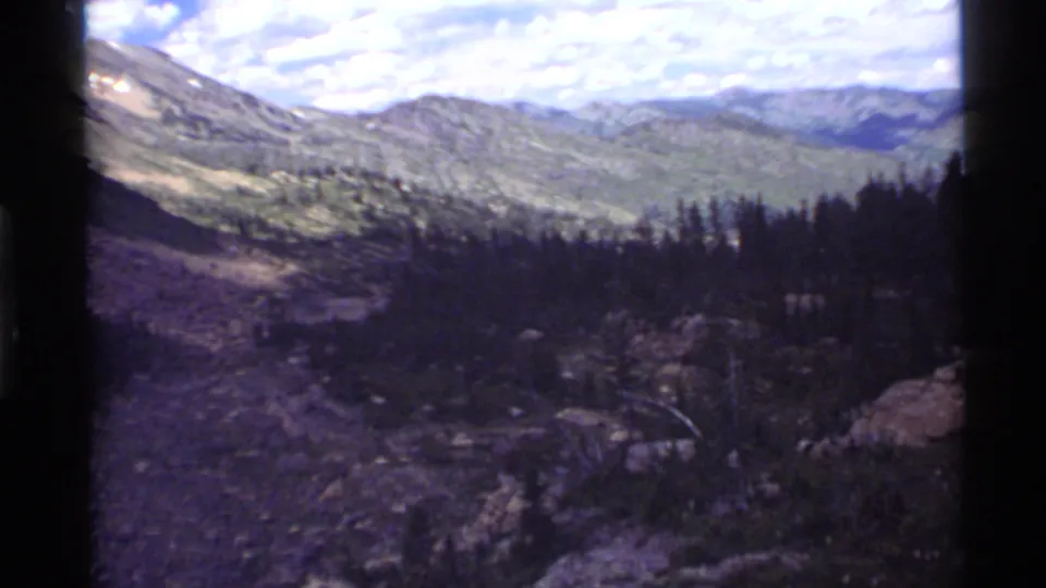 Holland Lake, Montana home-movie frame from 1972 showing a wide mountain vista, forested slope, rocks, and distant hills under clouds.