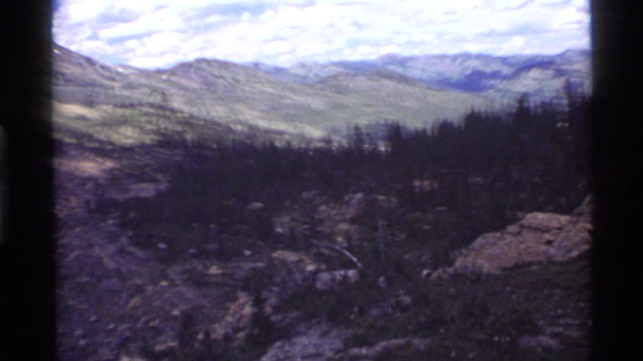 Forested mountain valley with rocky slopes under a partly cloudy sky.