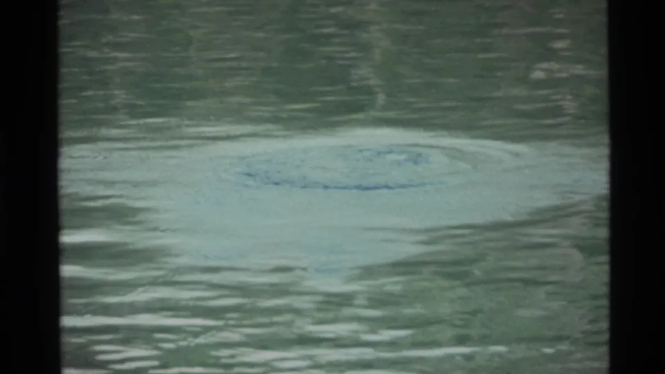 Holland Lake water in 1972 home-movie footage, showing a pale disturbance on the surface and dark scan borders.