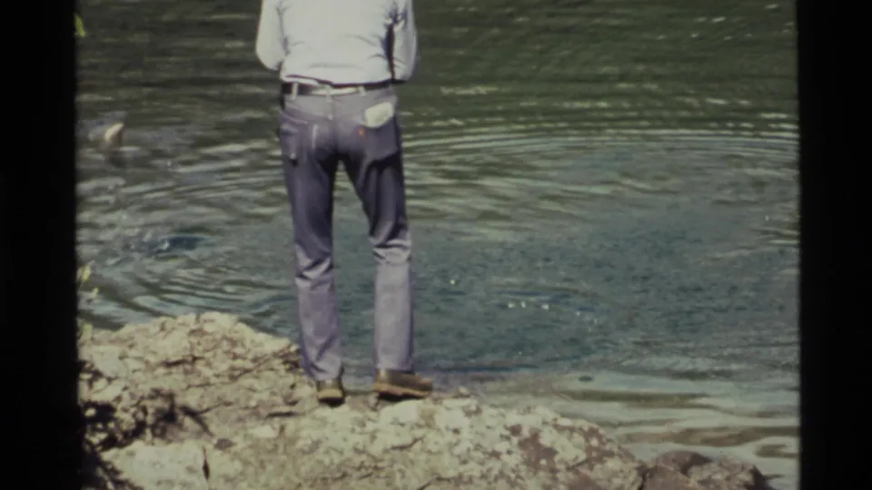 The man remains on the rocky lakeshore at Holland Lake as small disturbances and ripples mark the water in front of him.