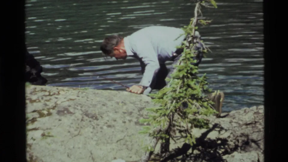 At the lakeshore, the fisherman drops to his hands or knees while recovering his balance near the water.