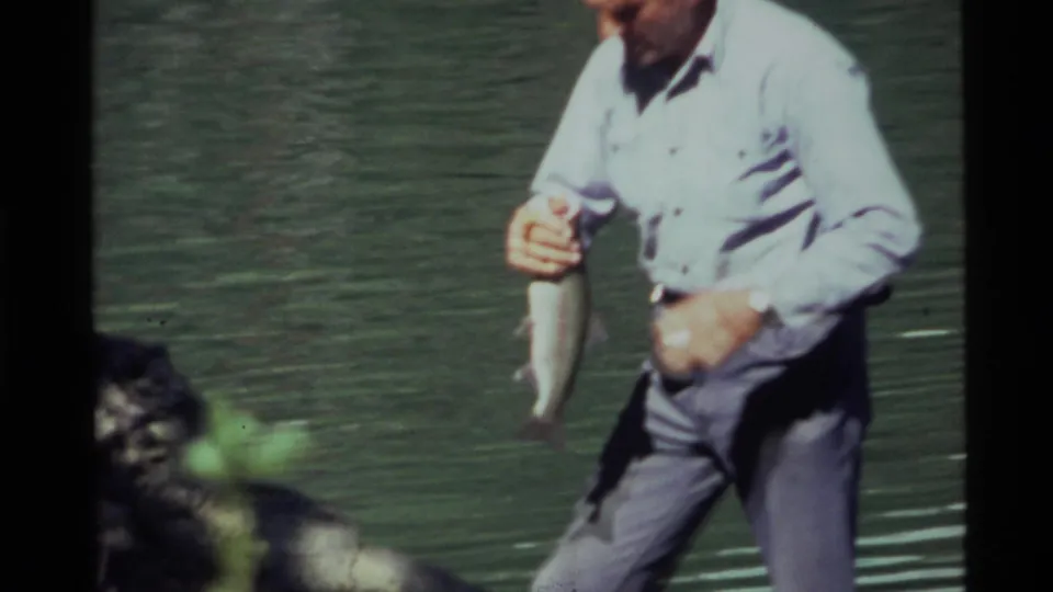 At Holland Lake in 1972, the man stands near the shore and grips the fish with lake water behind him.