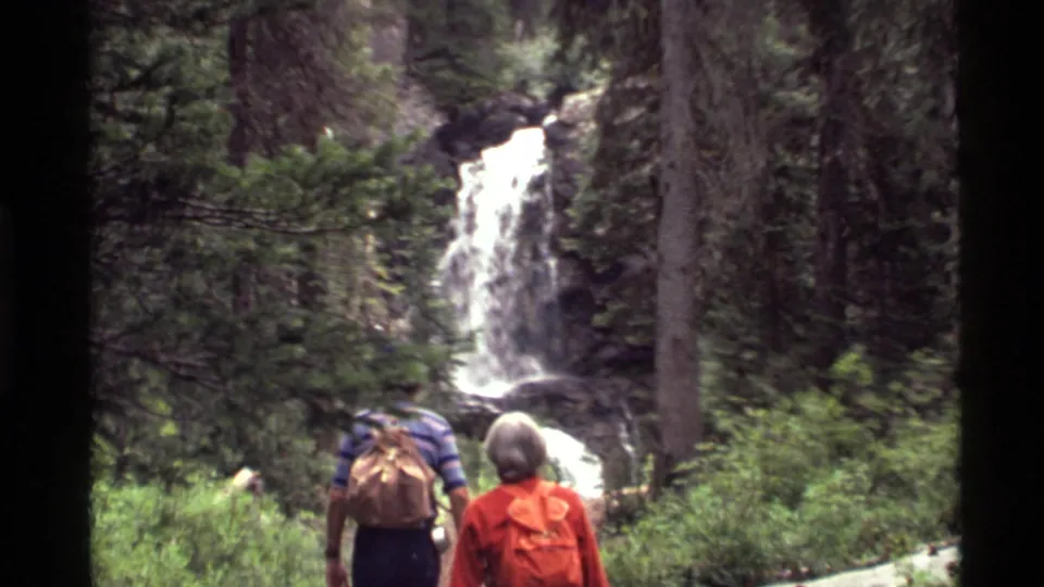 The 8mm frame shows the hikers closer to the waterfall, partly framed by trees and green forest growth at Holland Lake.