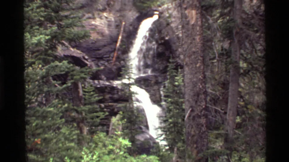 1972 Holland Lake, Montana home-movie frame with a closer view of cascading water among conifers and rock ledges.