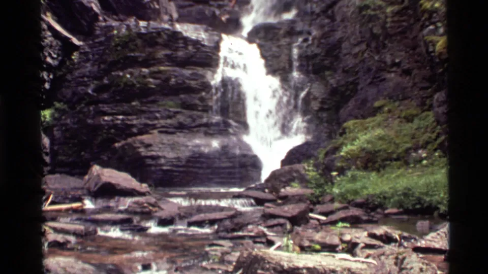 Lower tier of the Holland Lake waterfall, with water dropping into a shallow rocky stream below dense forest growth.