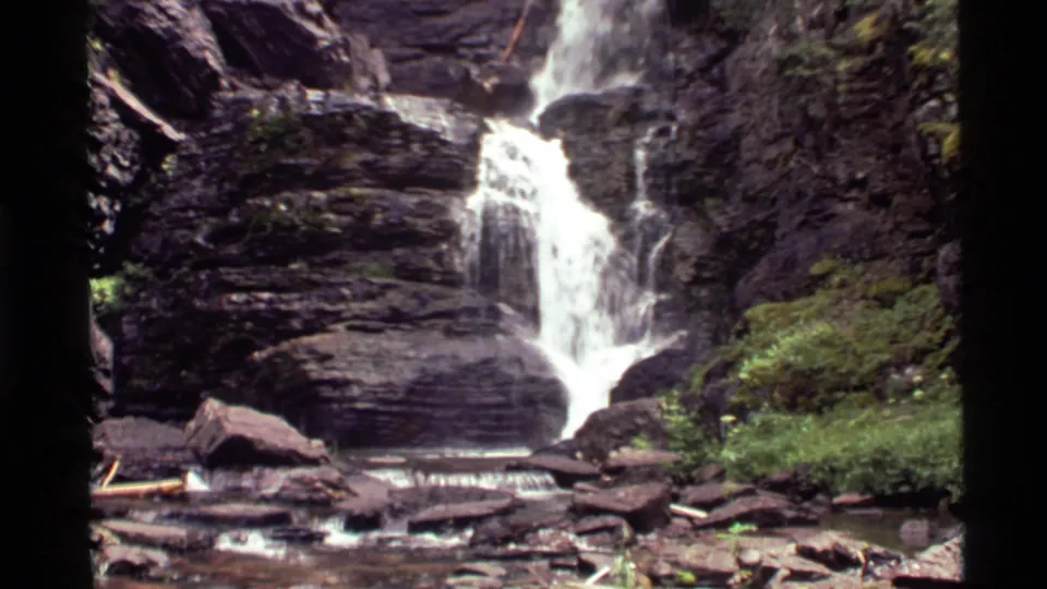 Final 1972 8mm frame of the Montana waterfall, showing the lower cascade, rock basin, stream water, and forest vegetation.